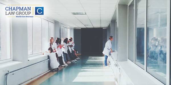 Doctors and nurses in a hallway of a hospital facing the windows on both sides.